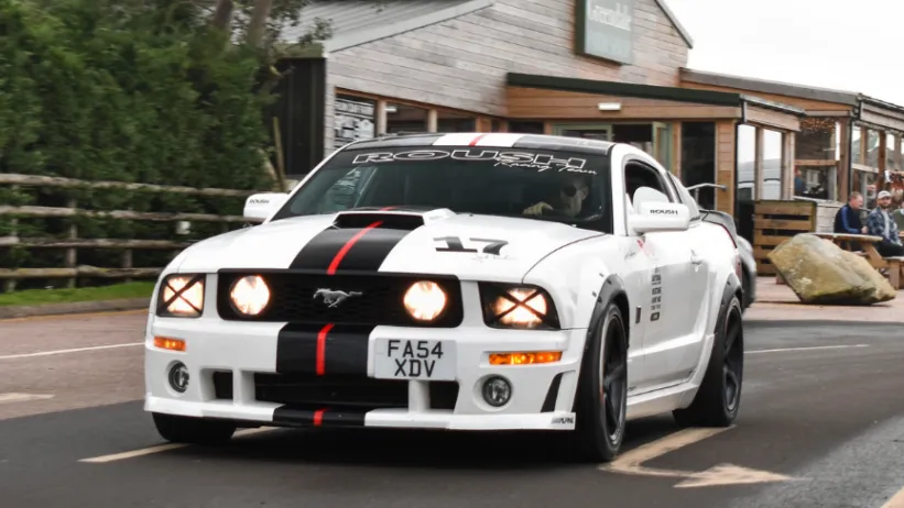 White Mustang GT v8 with black stripes in street with headlights on