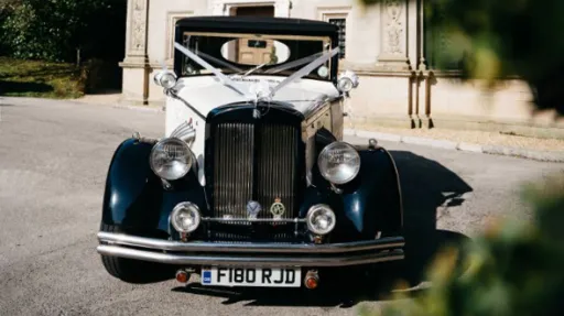 Full front view of vintage regent in black and white dressed with wedding ribbon decoration parked in front of a church