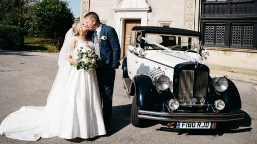 Black & White vintage style regent with Bride and Groom kiing next to the car. Church can be seen in the background