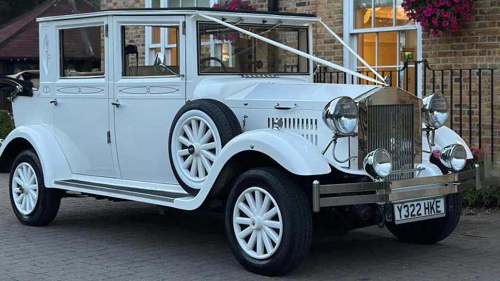 White vintage style imperial wedding car with rear convertible roof open, dressed with white ribbons, large wodden white wheels