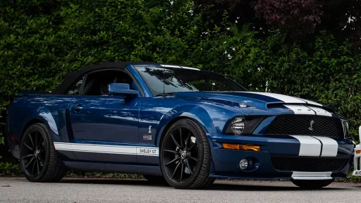 Blue ford Mustand Shelby with white stripes, black alloy wheels and black soft-top convertible rood