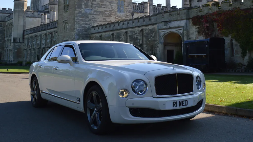 Front right side view of White Bentley Mulsanne with wedding venue in the background