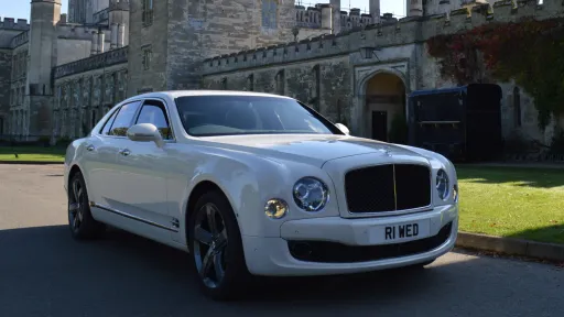 Front right side view of White Bentley Mulsanne with wedding venue in the background