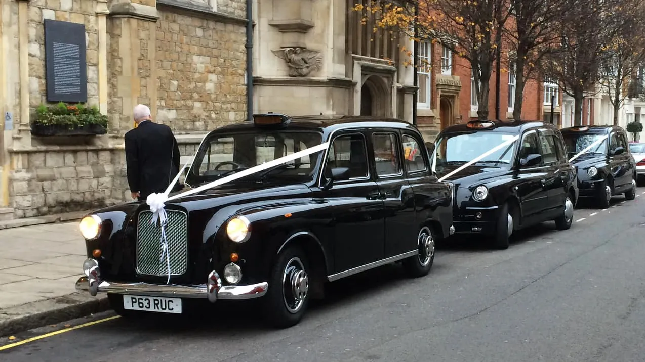 Fleet of Classic and Modern Black Taxicabs decorated with matching white wedding ribbons and bows parked in front of a church