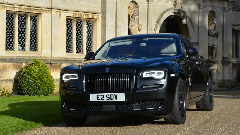 A Modern Black Rolls-Royce Ghost Series 2 with black alloy wheels parked in front of a wedding venue