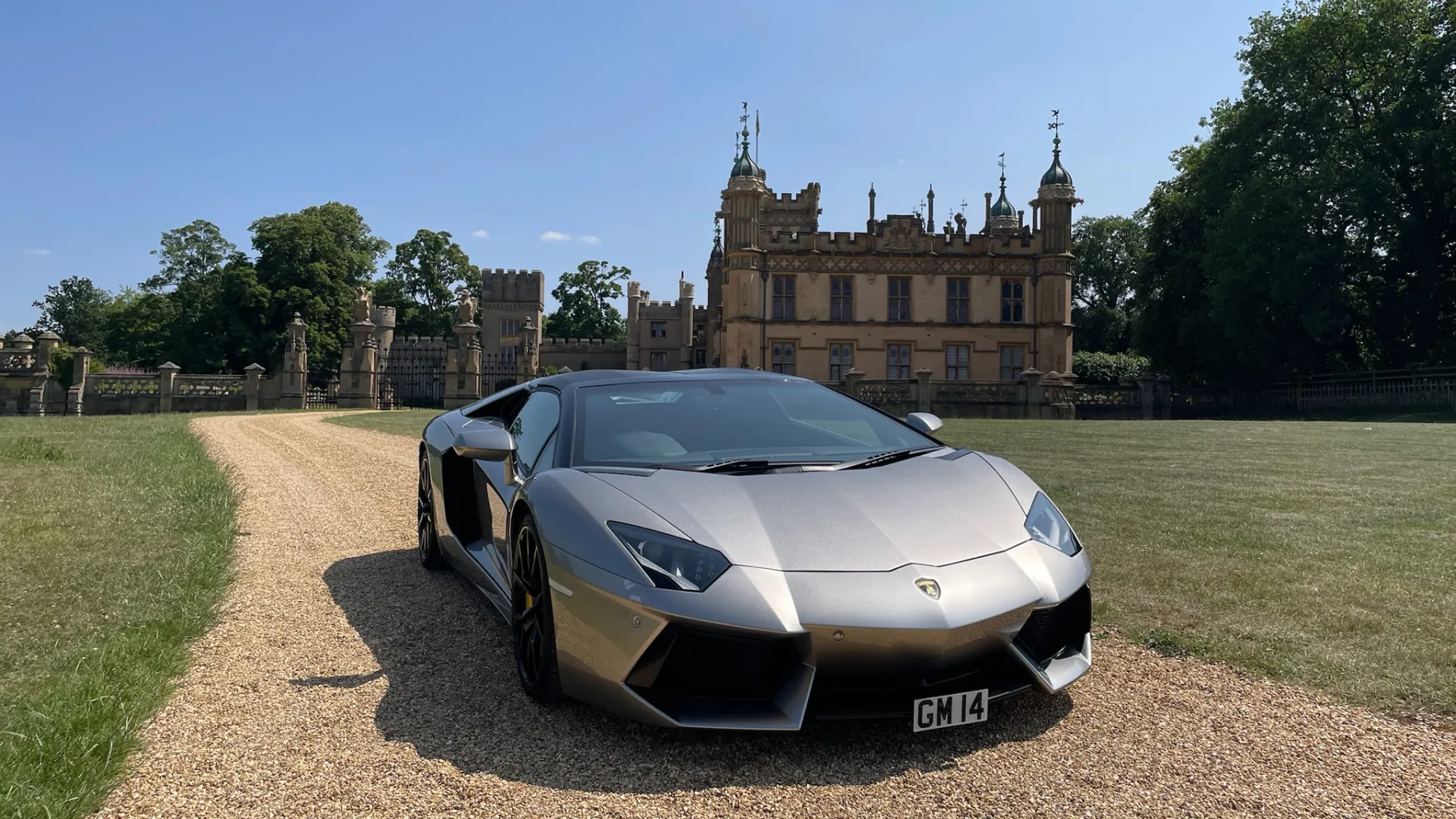 Silver Lamborghini Aventador wedding car parked on a gravel driveway in front of a historic castle venue, perfect for luxury and stylish grooms' wedding transport in the UK.