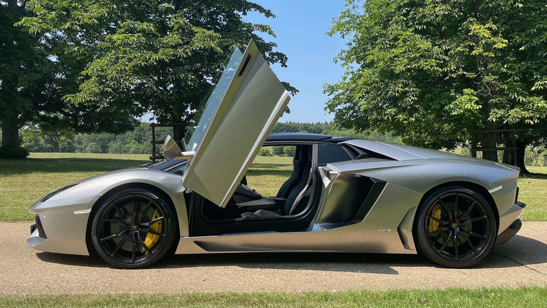 Side profile of a silver Lamborghini Aventador with upward-opening doors, showcasing its sleek design