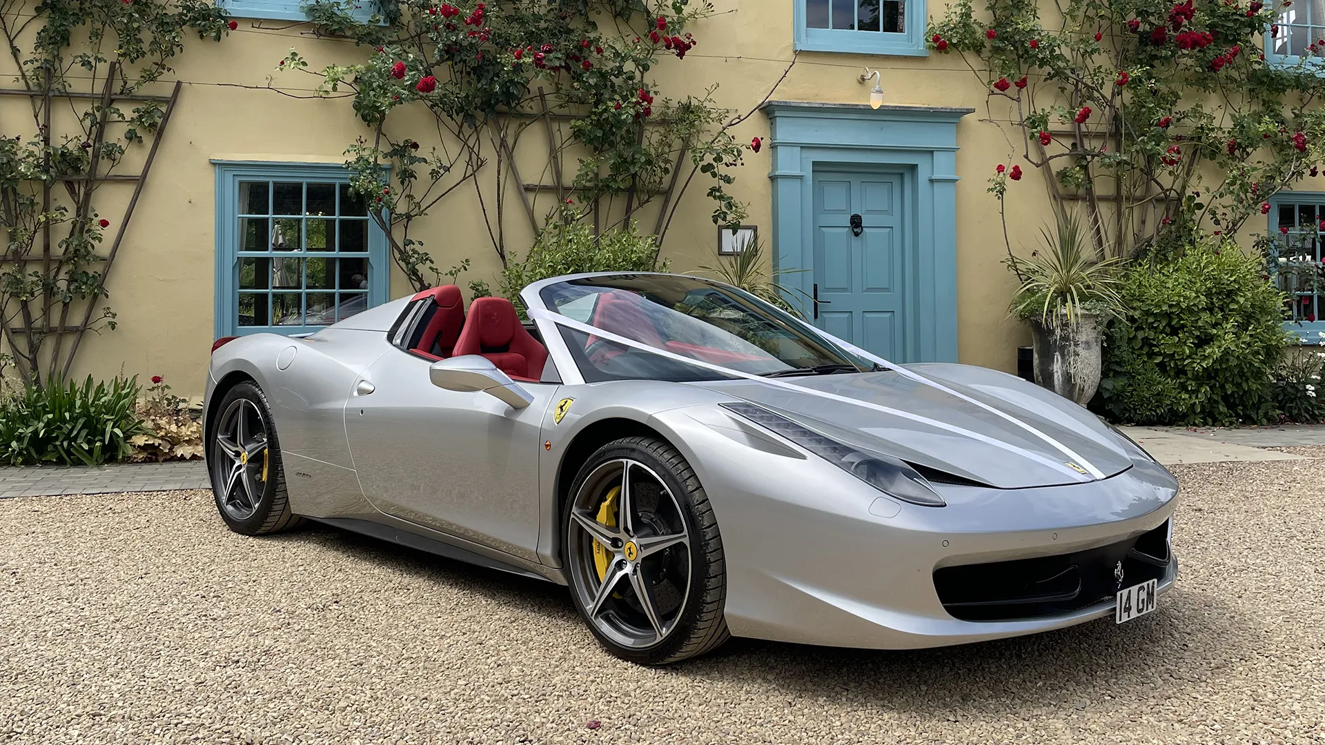 silver Ferrari 458 Spider convertible with red leather interior, parked outside a country house adorned with climbing roses and turquoise-painted doors