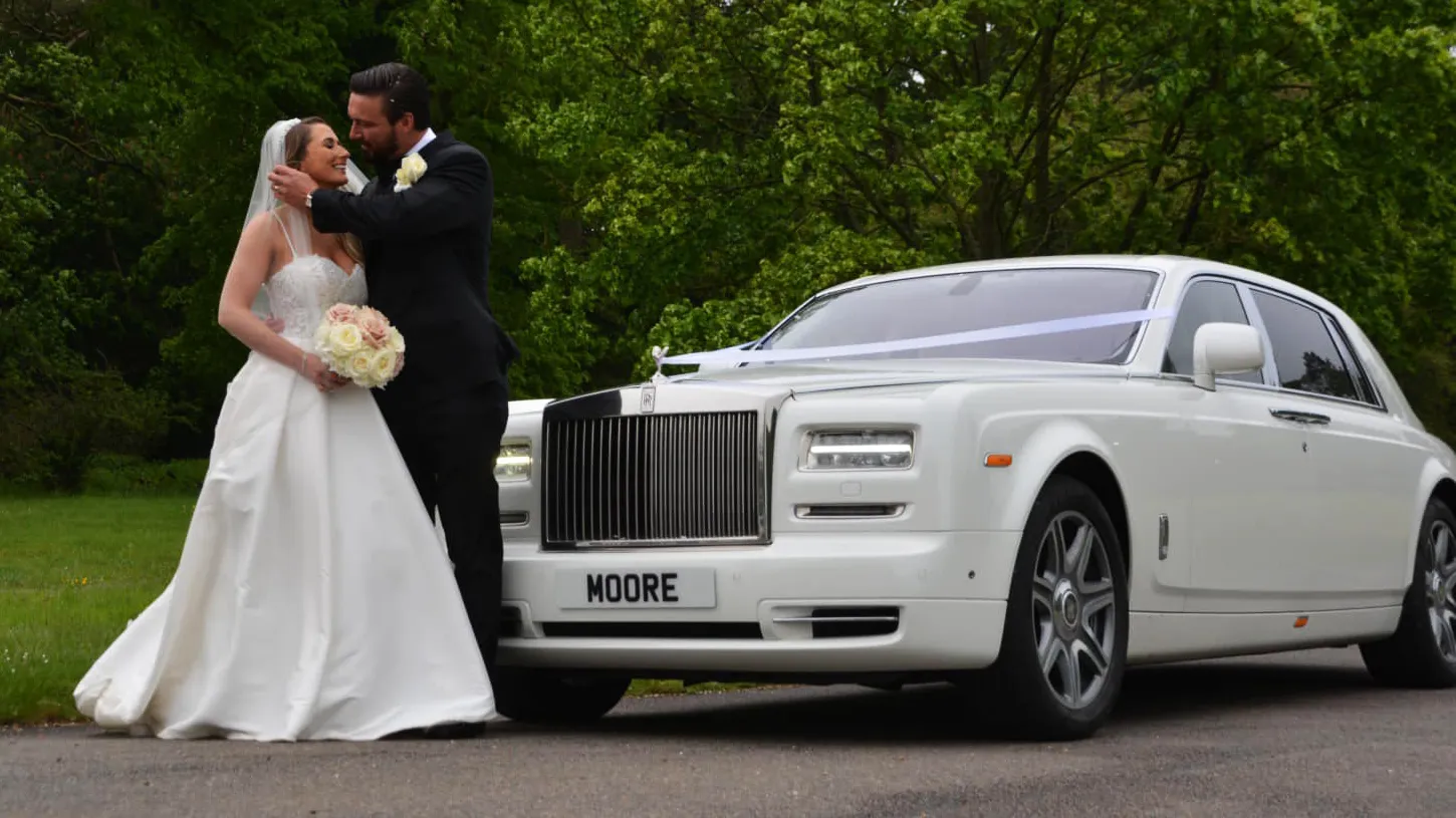 Bride wearing a white dressed with her groom standing in front of a White Rolls-Royce Phantom
