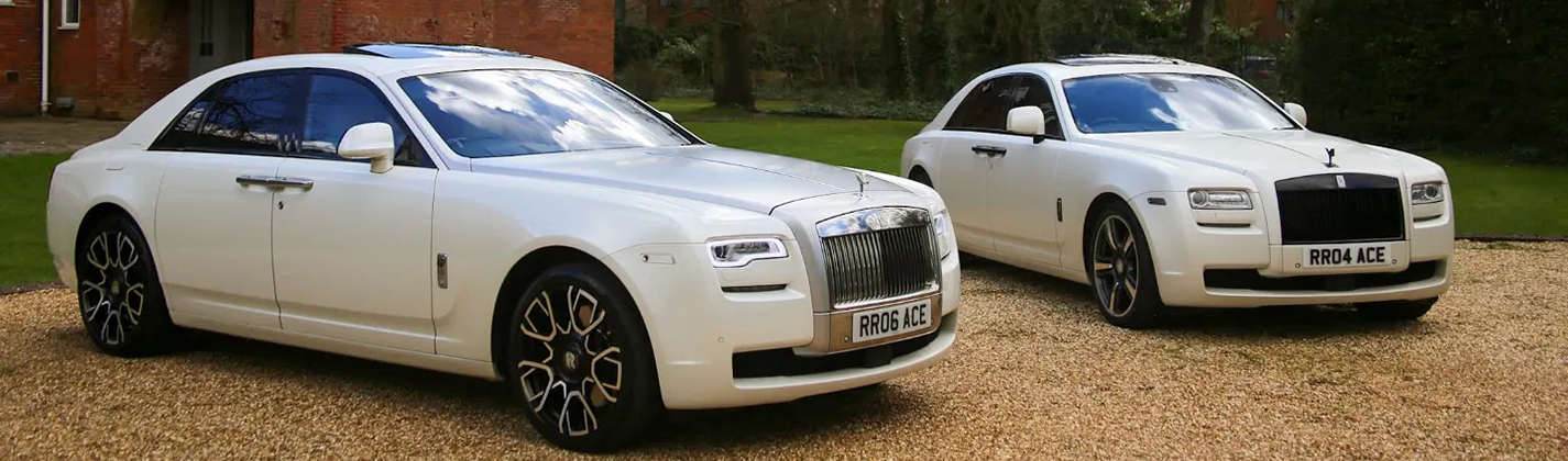 Two matching white Rolls-Royce Ghost parked next to each other's on a gravel entrance in front of a wedding venue