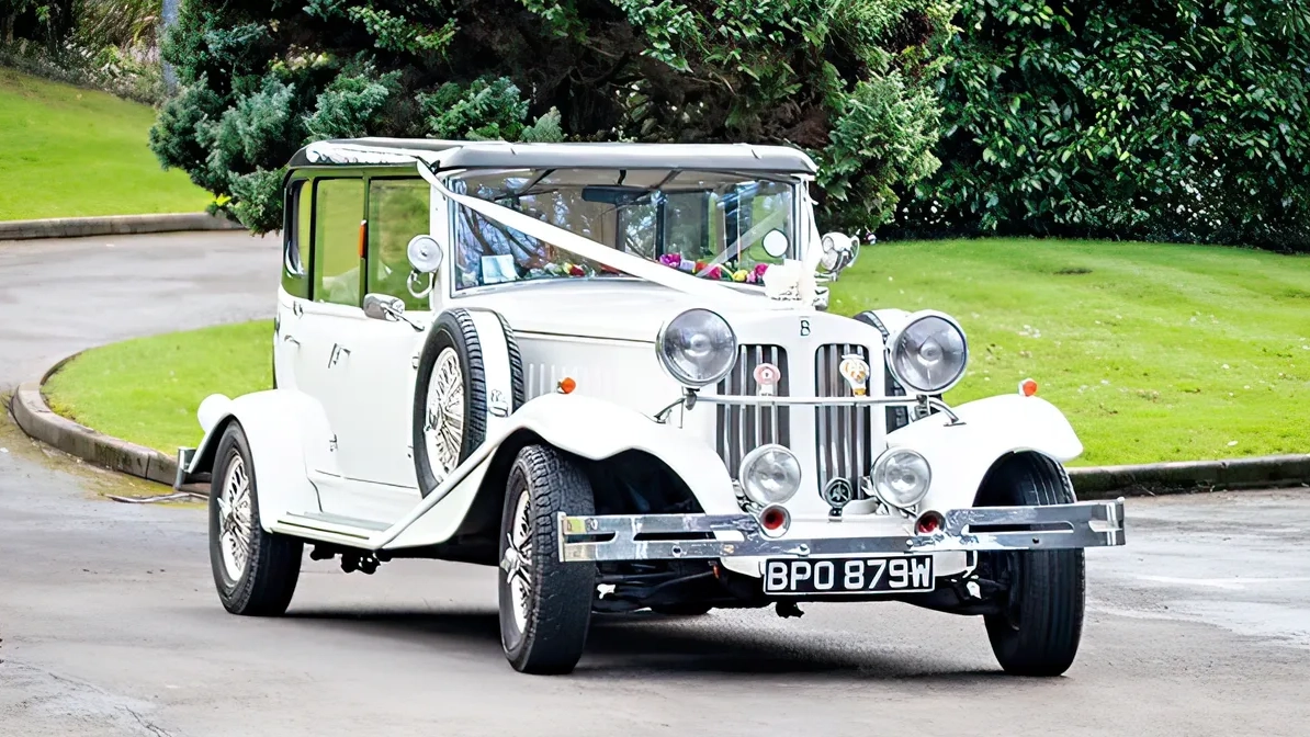 Vintage Beauford with white ribbons entering wedding venue