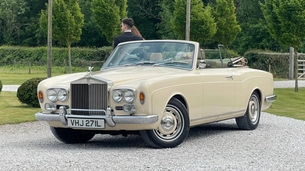 Rolls-Royce Corniche in Ivory with convertible roof open parked on a gravel path with greenrery in back ground
