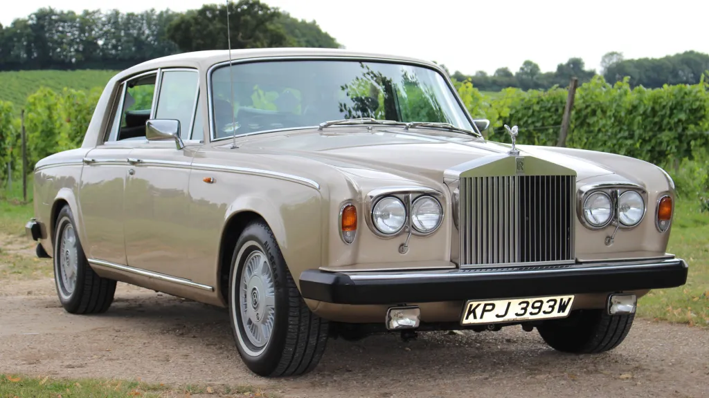Champagne gold coloured classic Rolls-Royce Silver Shadow with black front bumper and large chrome grill with spirit of ecstasy atop