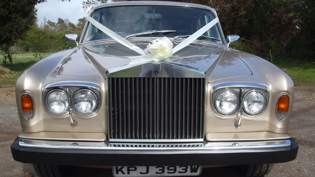 close-up front chrome grill view of Rolls-Royce Silver Shadow with white ribbons and large white bowe on top