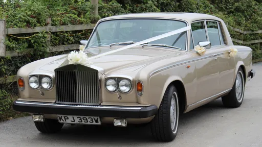 left side front view of Champagne gold coloured classic Rolls-Royce Silver Shadow dressed with wedding ribbons