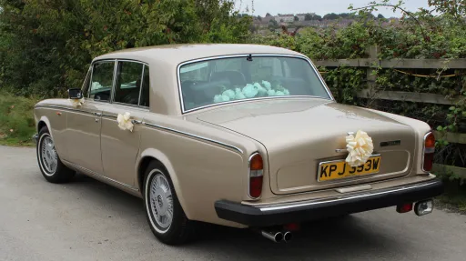 rear left side view of Rolls-Royce Silver Shadow in Champagne Gold with white ribbonsd on door handles and posy of white flowers on rear parcel shelf