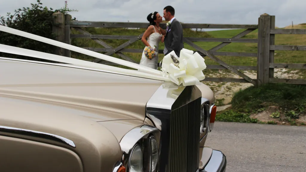 close up view of Rolls-Royce Silver Shadow front grill with large bow on top and Briode and Groom in the background