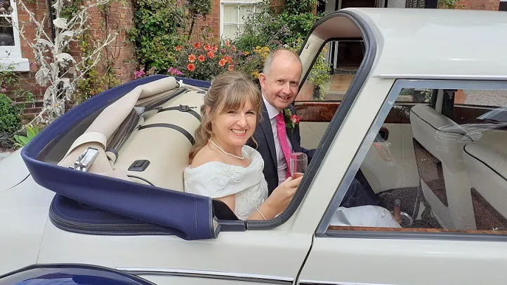 Bride and Groom seating inside vintage-style Royale windsor wedding car with roof down posing for photos