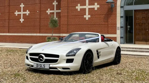 White Mercedes SLS AMG fron side view decorated with Lillac ribbons parked in front of an Asian Temple