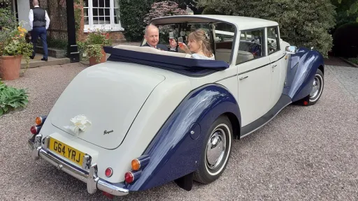 Rear view of vintage-style Royale Windsor with semi-convertible roof open showing happy couple seating inside the vehicle