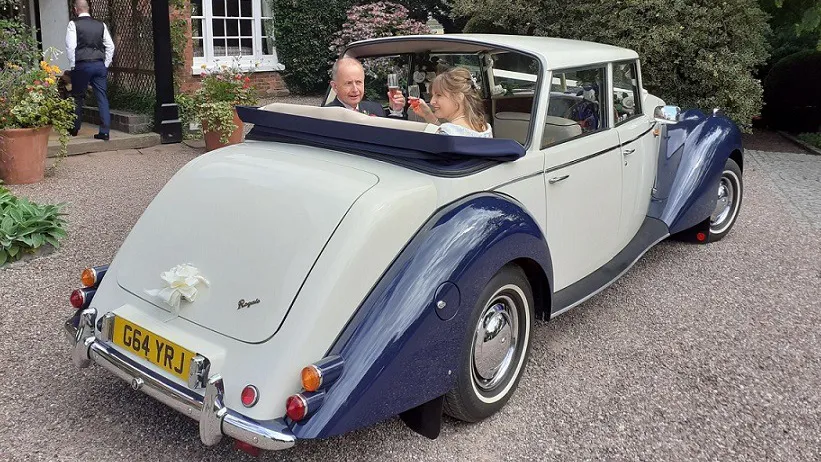 Rear view of vintage-style Royale Windsor with semi-convertible roof open showing happy couple seating inside the vehicle