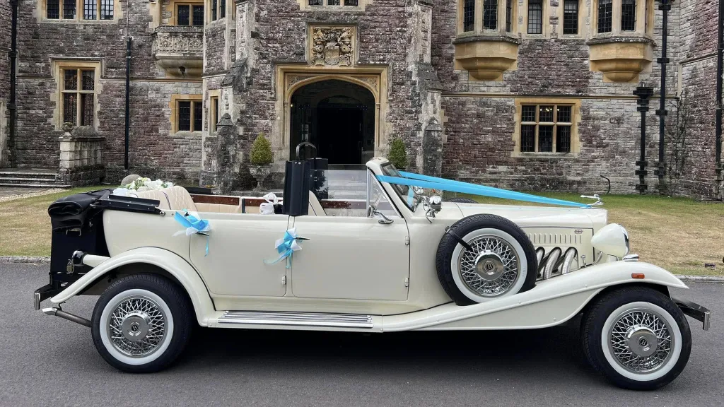 Ivory Beauford convertible with roof open, turquoise ribbons and bows on door handles parked in front of Rhinefield House in New Forest