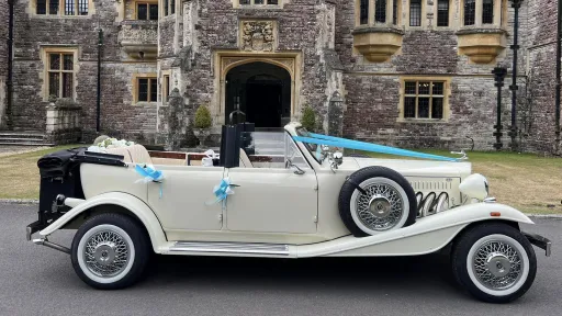 Ivory Beauford convertible with roof open, turquoise ribbons and bows on door handles parked in front of Rhinefield House in New Forest