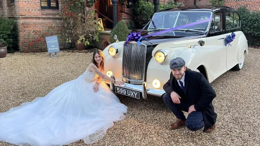 Austin Princess Limousine in Ivory with headlights switched on. Both Bride and Groom and kneeled down in front of the vehicle