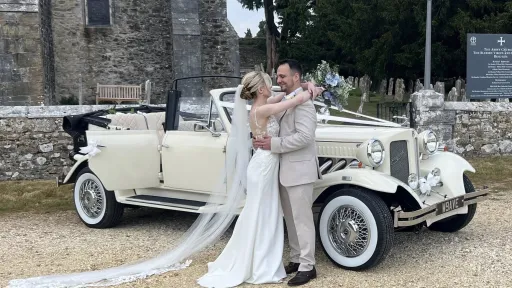Bride and Groom holding each others and standing next to a Vintage beauford Convertible with Church in the background
