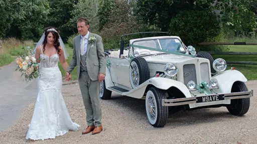 Bride and Groom holding hands in front of a vintage style Ivory Beauford Convertible