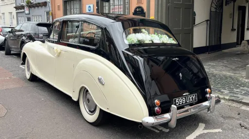 Rear view of Ivory Austin Princess Limousine with black roof and boot parked in the street of Southampton with view of the floral arrangmennt on the rear parcel shelf through the rear window