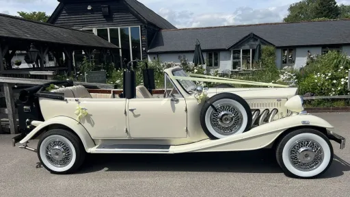 Right side veiew of Beauford convertible with convertible roof fully open, yellow ribbons and bows. Parked on front of a wedding venue
