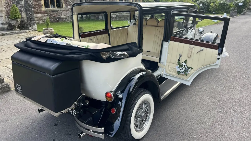 Rear right view of Bramwith convertible car with rear door open, black picnic trunk at the rear and cream leather interior with floral decoration inside the vehicle