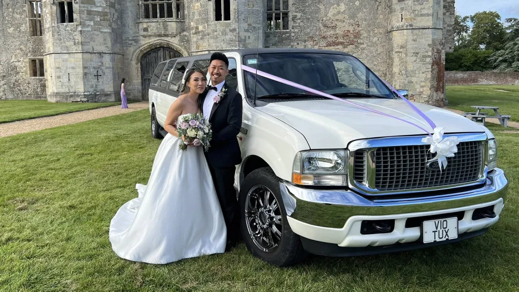 Ford Excursion Stretched Limousine in white with Brideand Groom holding each others next to the limo