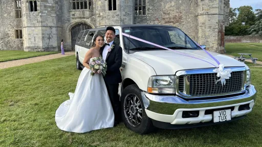 Ford Excursion Stretched Limousine in white with Brideand Groom holding each others next to the limo