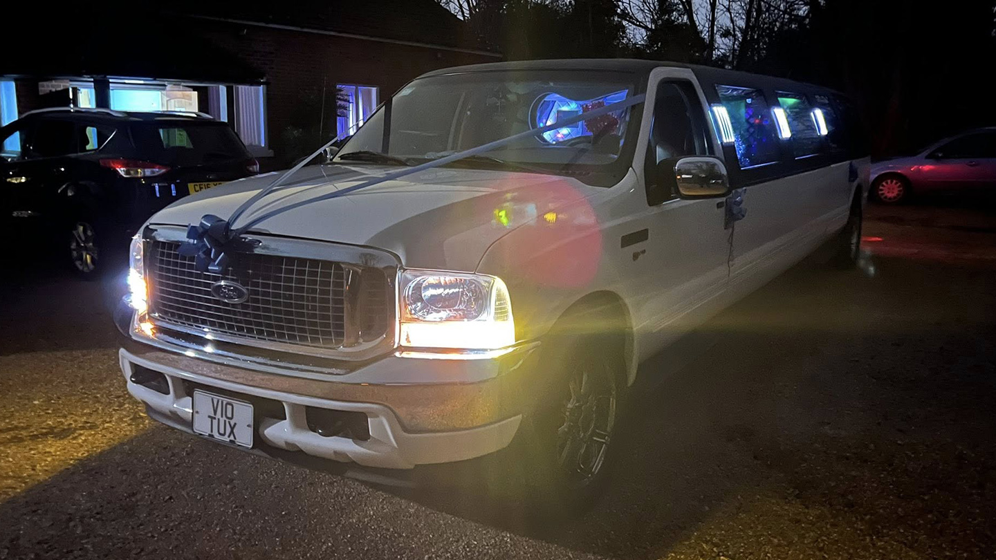 Ford Excursion Stretched Limousine parked outsidea venuw at night time with illimunated lights.