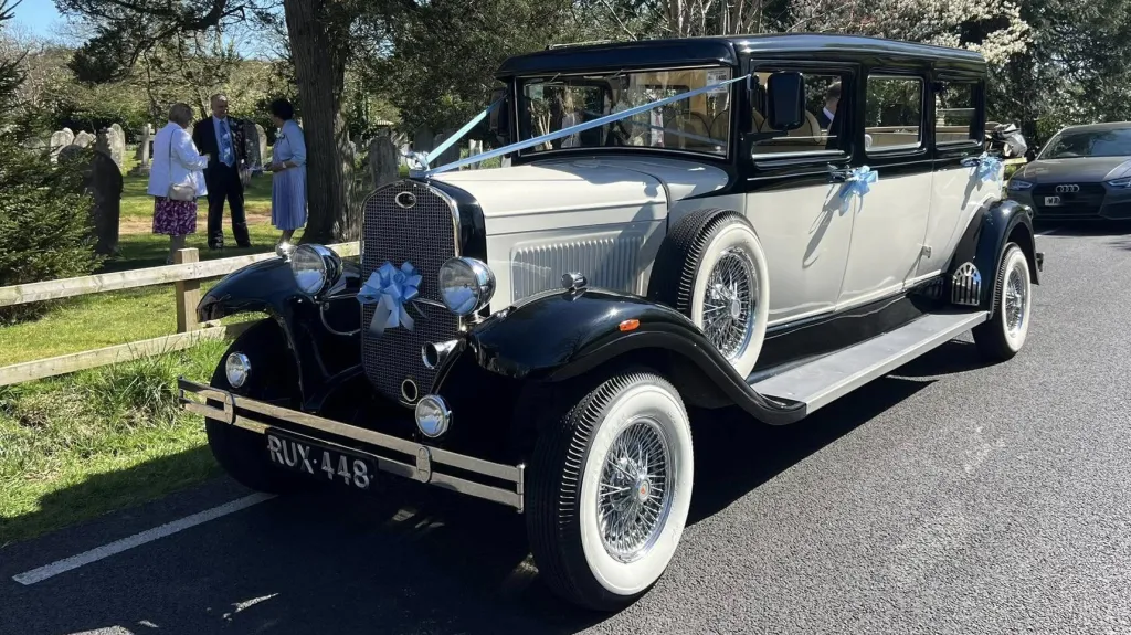 Left side view of Bramwith in Ivory and Black with wedding decoration and spare wheel mounted on the left side of the vehicle. Parked in front of a church with wedding guests in the background