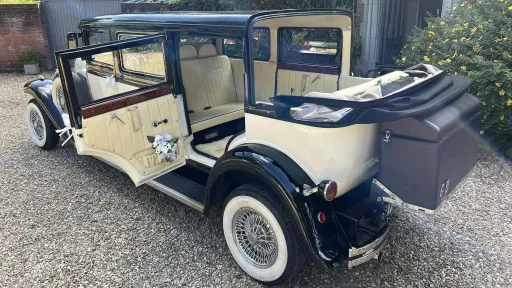 LKeft side view of vintage-style Bramwith with convertible roof open, cream leather interior, white flower decoration inside the vehicle