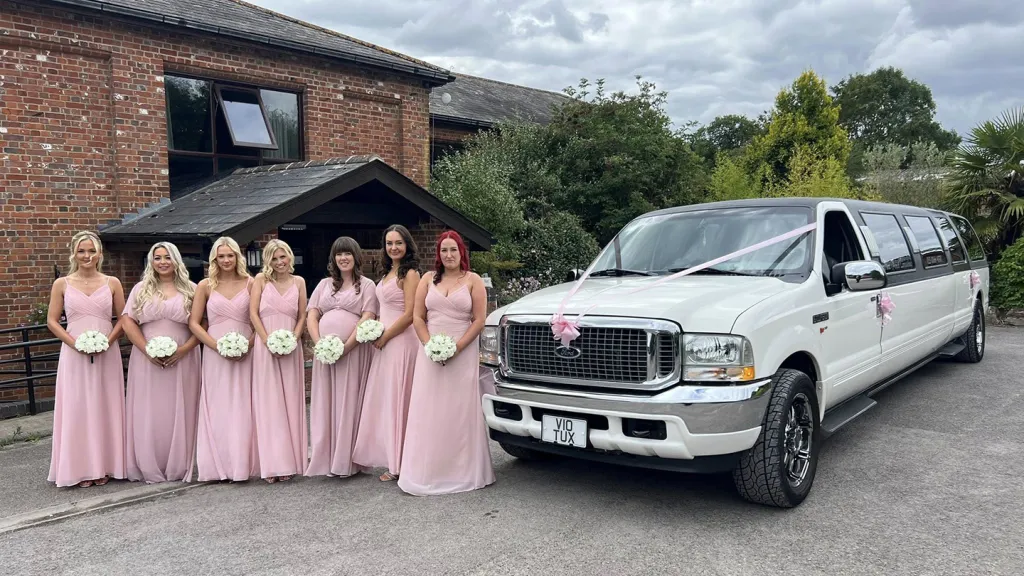 7 ?Bridesmaids wearing light pink dresses standing next to a white Ford stretched limo