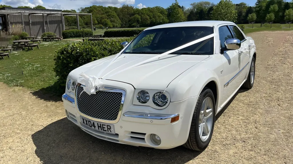 White Chrysler 300c saloon car parked at a wedding venue decorated with white ribbons