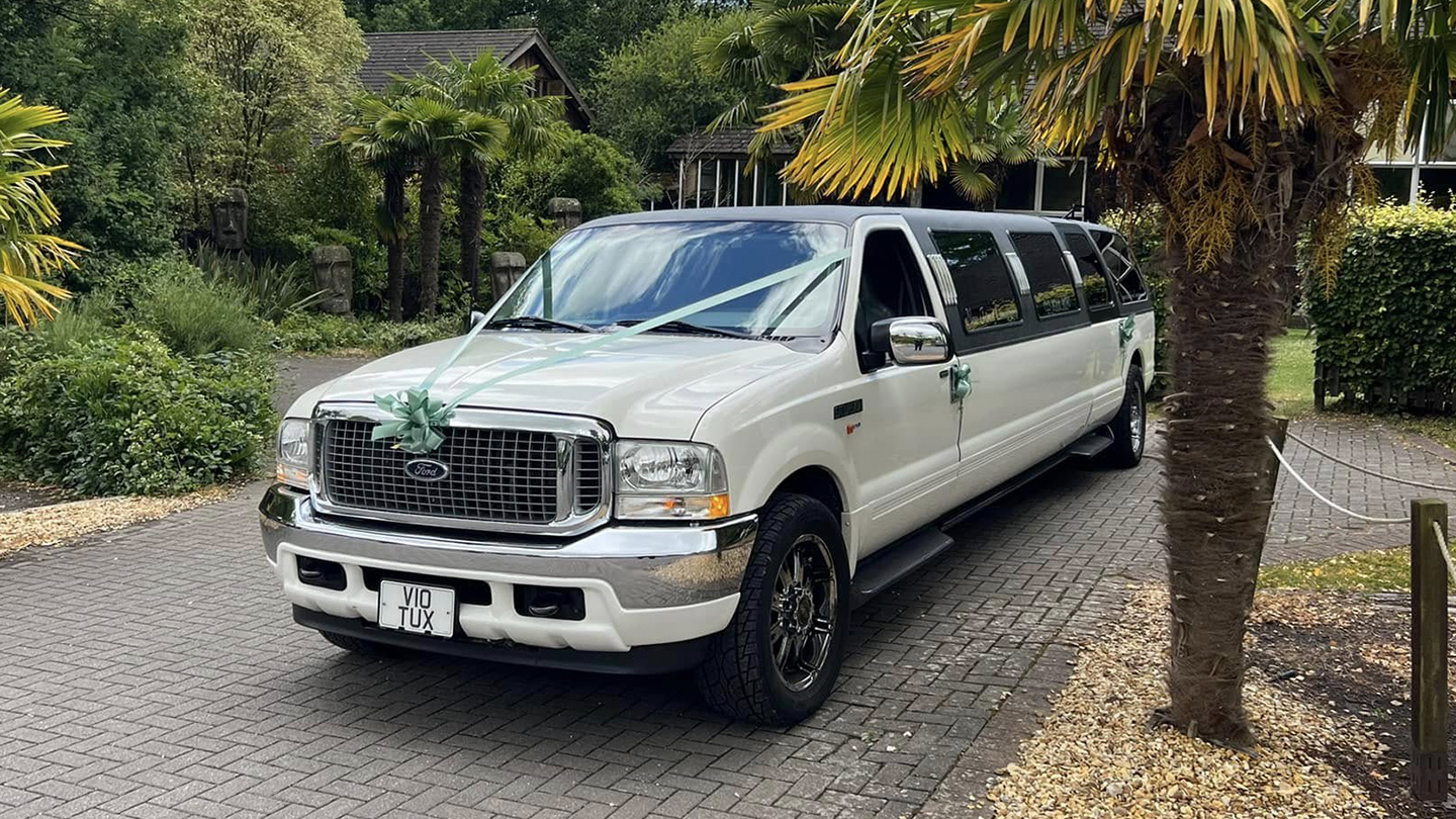 Ford Excursion Stretched Limousine dressed with green ribbons and bows parked at a wedding venue with palm trees