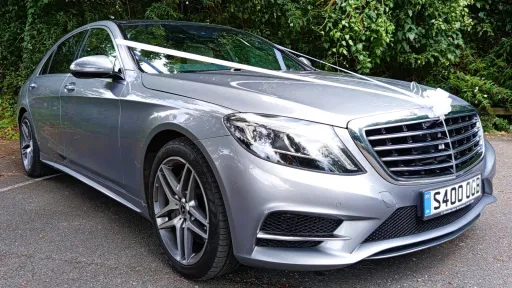 Silver Mercedes S-class dressed with white wedding ribbons across the bonnet and a white bow on top of the chrome grill
