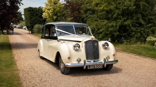 Classic Ivory Austin Princess Limousine with black roof and decorated with white ribbons and bows entering a wedding venue in Leicester
