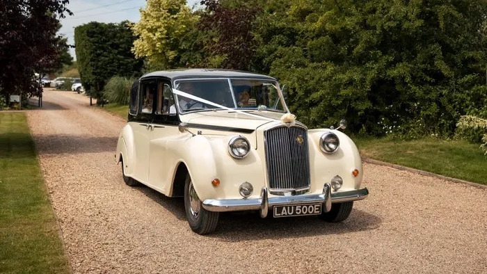 Classic Ivory Austin Princess Limousine with black roof and decorated with white ribbons and bows entering a wedding venue in Leicester