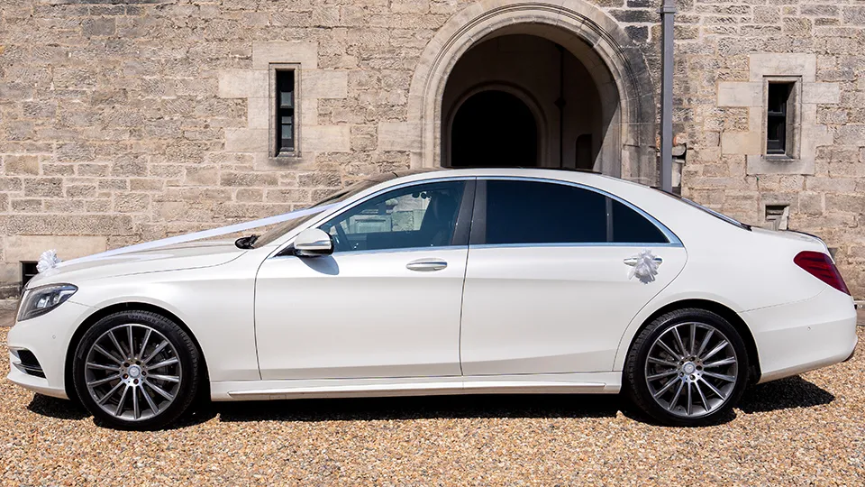 Roght side view of a white mercedes dressed with ribbons pasrked in front of a castle-like wedding venue in Aberdeen