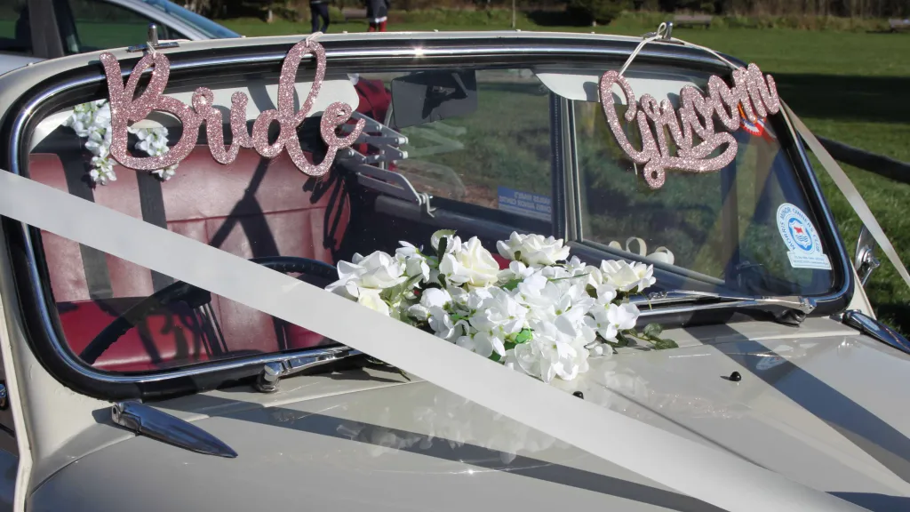 Classic Morris Minor Convertible with wedding decoration and a pink parkling Bride and Groom sign at the front