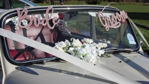 Classic Morris Minor Convertible with wedding decoration and a pink parkling Bride and Groom sign at the front
