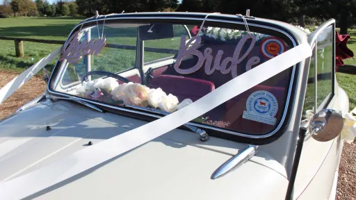 Classic Morris Minor with convertible roof open and pink Bride and Groom sign attached to the vehicle