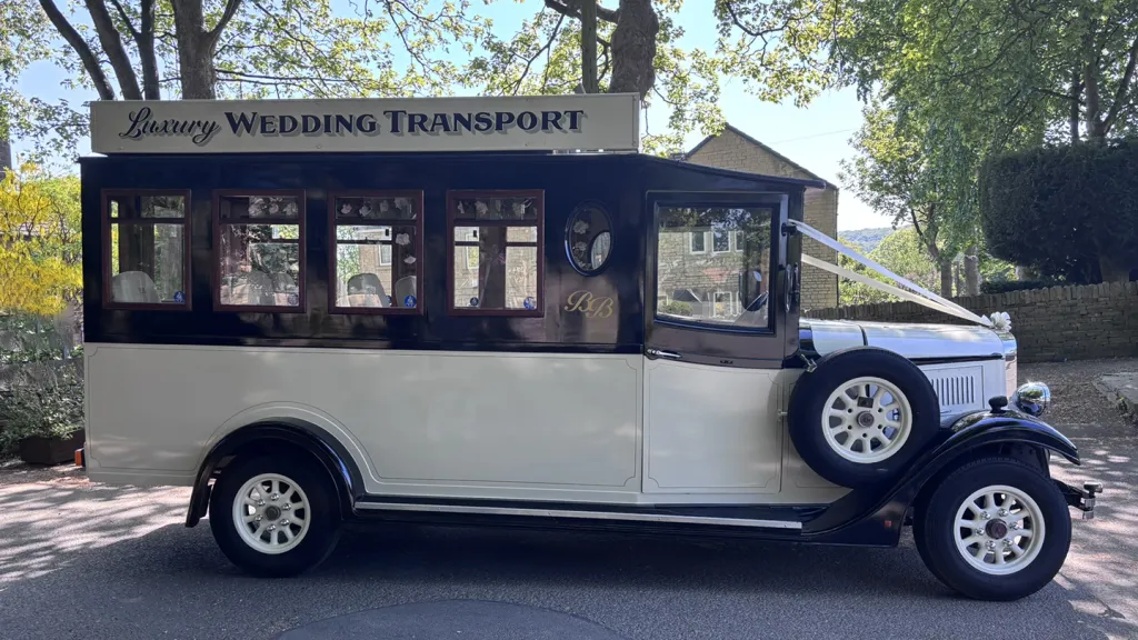right side view if black and ivory Asquith Bus with spare wheel mounted on the side of the bus. Green trees in the background