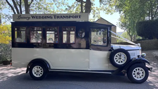 right side view if black and ivory Asquith Bus with spare wheel mounted on the side of the bus. Green trees in the background
